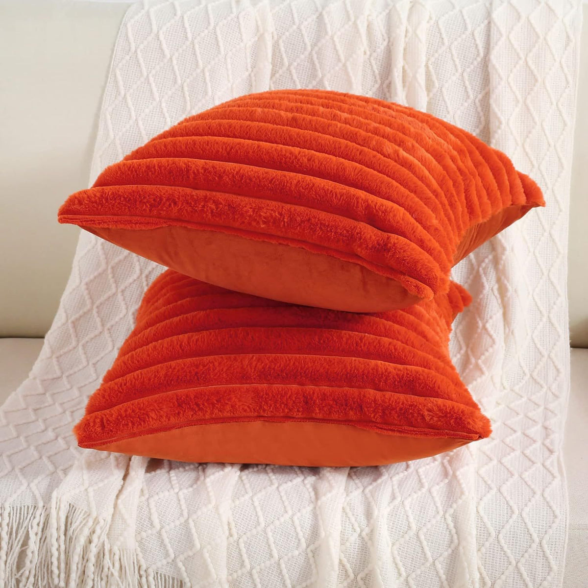 Verdelisse faux fur throw pillow covers in Orange, two covers stacked on a white knit throw