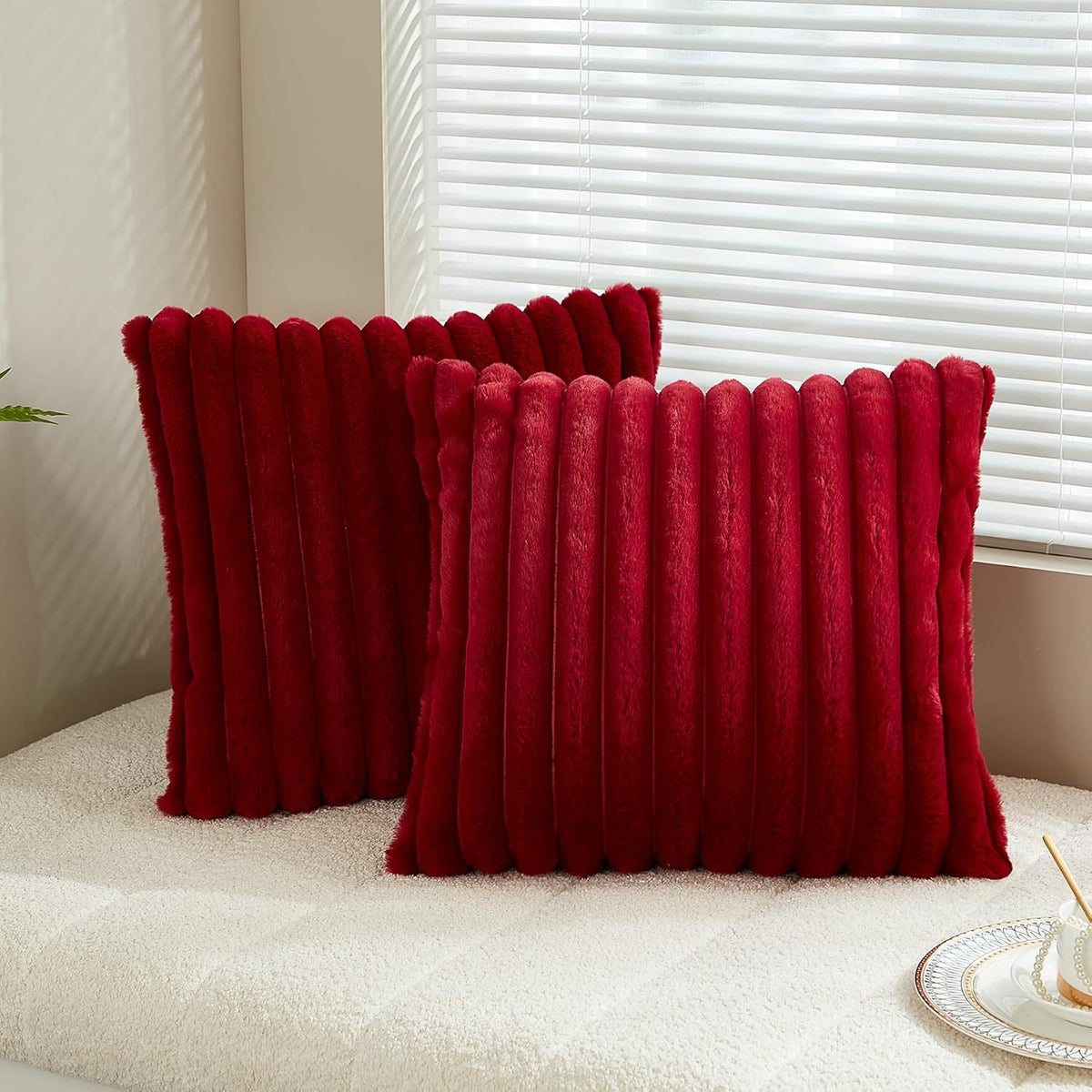 Verdelisse faux fur throw pillow covers in Burgundy, a pair on a white sofa by the window