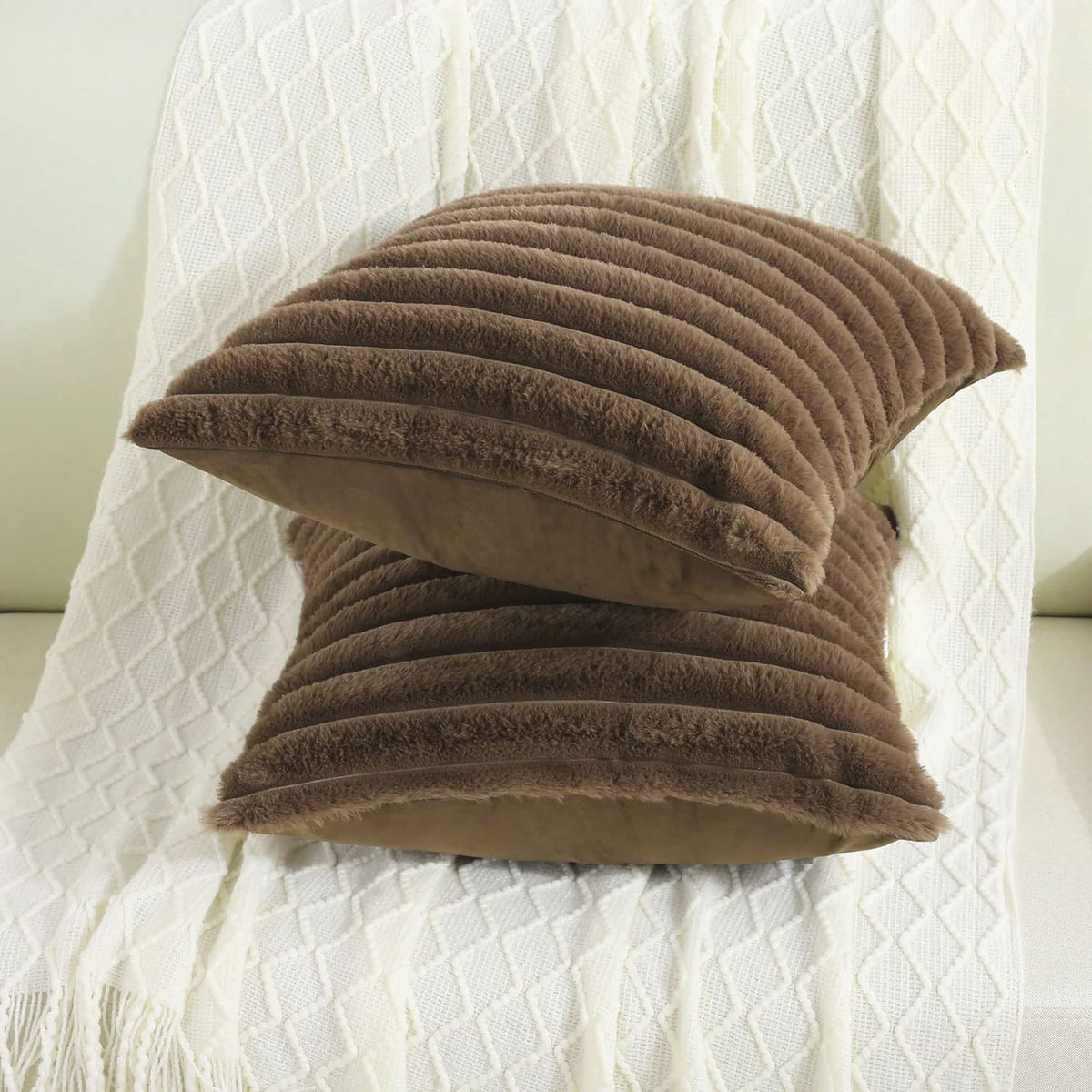 Verdelisse faux fur throw pillow covers in Brown, two covers stacked on a white knit throw