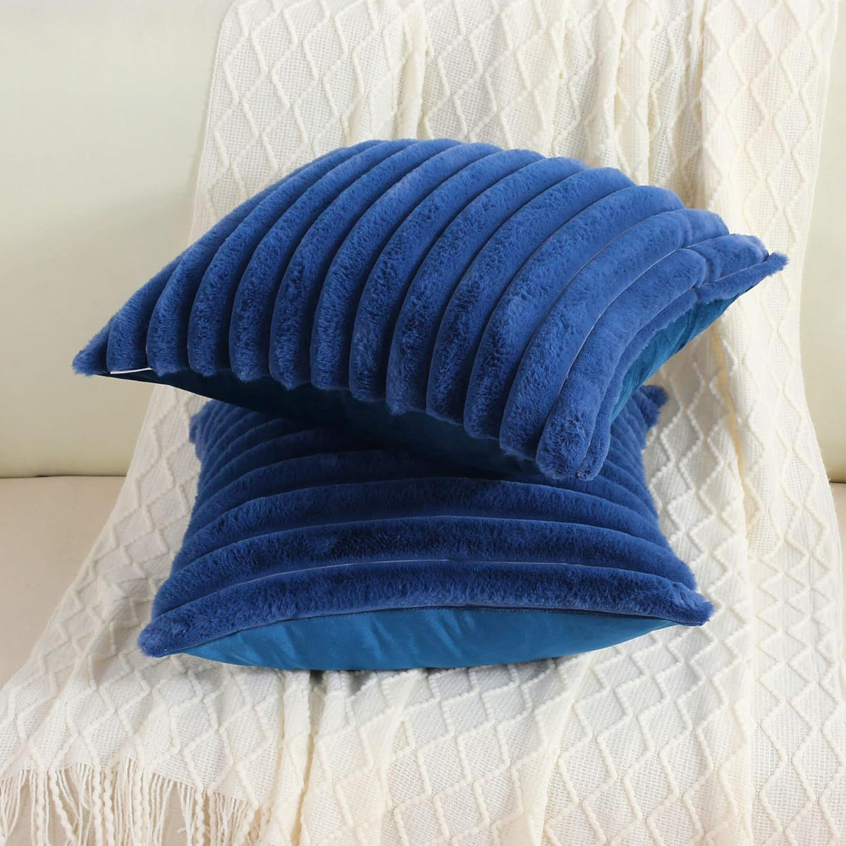 Verdelisse faux fur throw pillow covers in Royal Blue, two covers stacked on a white knit throw
